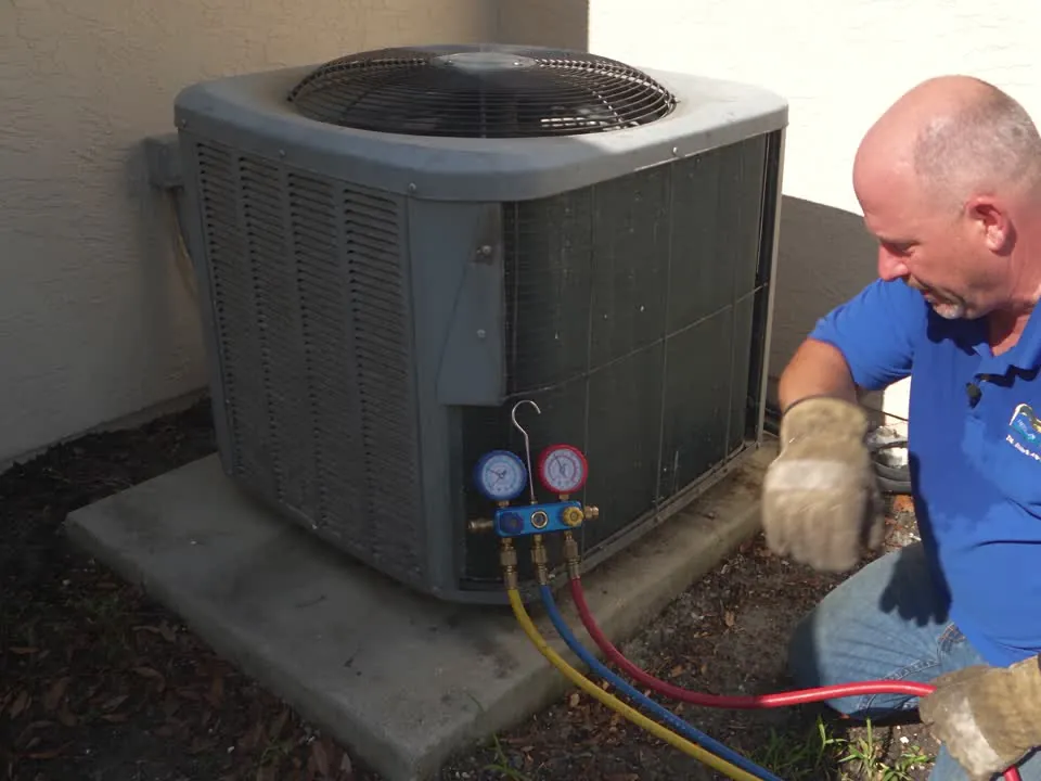 A technician reads refrigerant gauges connected to an outdoor AC unit